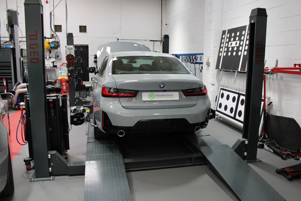 A gray BMW car on a hydraulic lift in a well-equipped automotive workshop, showcasing vehicle maintenance and inspection equipment.