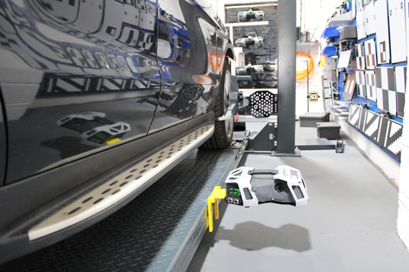 A close-up view of a black vehicle on a lift with a measuring device positioned near the tire, showcasing a modern automotive workshop setting.