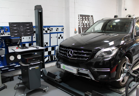 A black Mercedes SUV parked in a vehicle diagnostics workshop, with a computer station displaying diagnostic tools and equipment in the background.