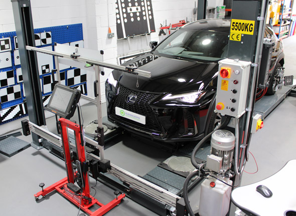 Black Lexus vehicle positioned on a workshop lift, surrounded by calibration equipment and tools in a modern automotive environment.