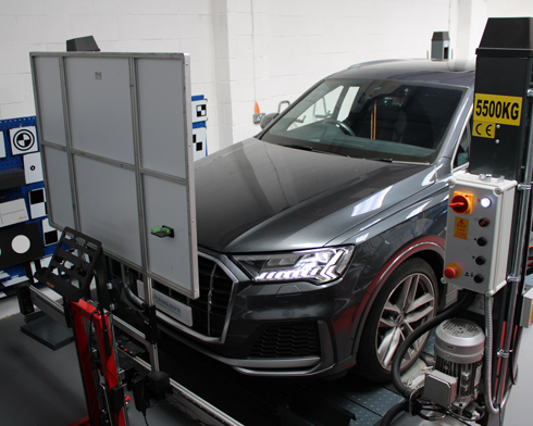 A gray Audi Q7 parked in a vehicle testing facility with diagnostic equipment and a weight display.