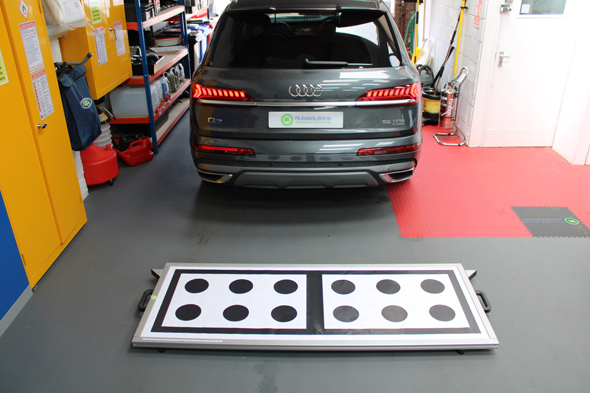 A gray Audi Q7 parked inside a garage with a device featuring black and white circles on the ground in front of it.