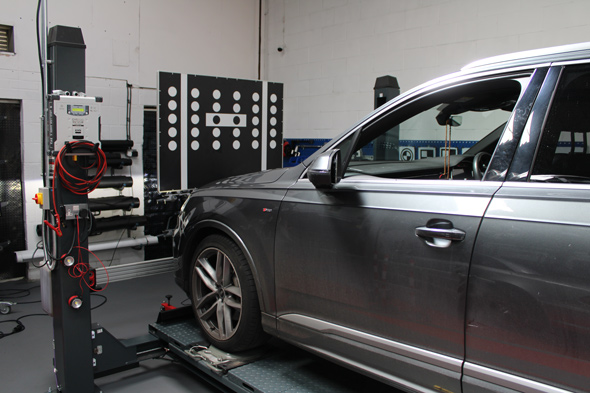 car undergoing alignment on a diagnostic platform in a workshop with equipment in the background