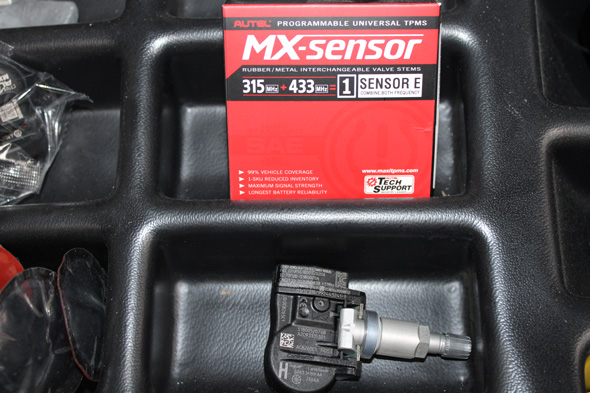 MX-sensor tire pressure monitoring system (TPMS) sensor with red packaging, featuring details such as frequency (315/433 MHz) and programmable features, set against a dark background.